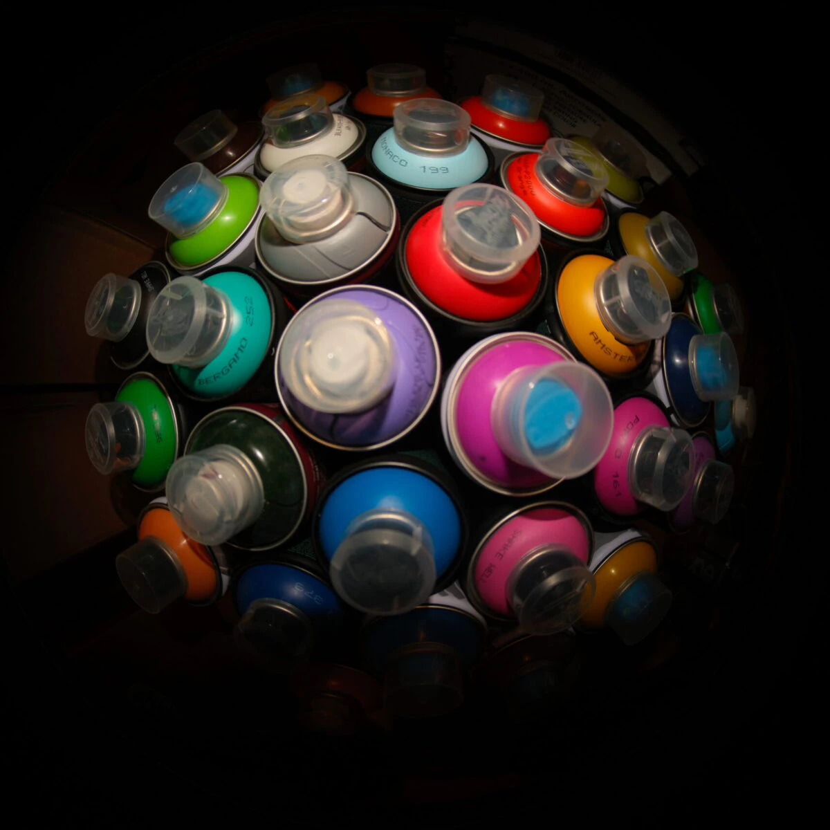 Viele Spraydosen von oben fotografiert, bunte Caps auf dunklem Hintergrund